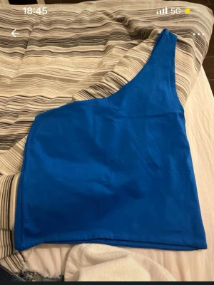 Blå oneshoulder topp - Snygg blå oneshoulder topp i stretchigt material. Enkel och stilren design utan mönster eller detaljer, perfekt att matcha med jeans eller kjol. Passar dig som gillar trendiga och unika snitt.