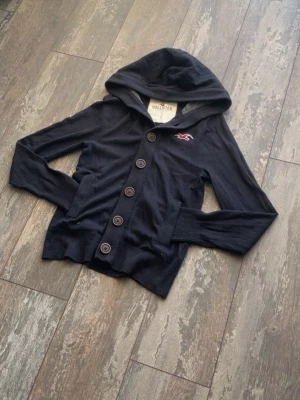 Hollister Cardigan Hoodie - Säljer en riktig snygg Hollister Cardigan Hoodie. Denna är väldigt välkänd och många som söker. Den är sällsynt och snygg. Skicket är 10/10. Storlek är S. Priset kommer ligga på 699kr.