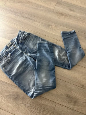Blå slim fit jeans med slitningar - Säljer ett par blå slim fit jeans med snygga slitningar och tvättade detaljer. Jeansen har klassisk femficksmodell, dragkedja och knapp i midjan. Perfekta för en avslappnad och trendig look.