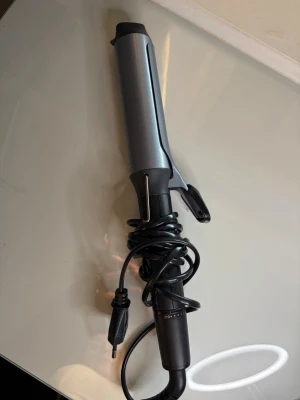 Locktång från Remington, svart/grå - Locktång från Remington i svart och grått med sladd och temperaturinställning. Utrustad med klämma och värmeskyddande spets. Perfekt för att skapa stora lockar och vågor i håret.