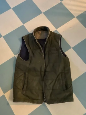 Stenström väst - Snygg mörkgrön dunväst med hög krage och dragkedja framtill. Västen har två fickor på sidorna och är fodrad för extra värme. Perfekt att slänga över en hoodie eller tröja när det är kyligt ute.