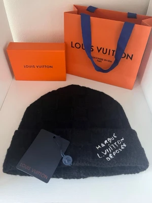 Svart   mössa - Snygg svart mössa från  med diskret rutmönste och broderad vit text ' framtill. Mössan är stickad och har en klassisk uppvikt kant. Perfekt accessoar för att lyfta din streetstyle. Helt ny oanvänd ✅