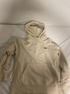 Beige hoodie från Levi's med huva - Säljer en beige hoodie från Levi's med klassisk huva och stor magficka. Tröjan har ribbade muddar vid ärmslut och nederkant, samt Levi's-logga på bröstet. Materialet är mjukt och bekvämt, perfekt för chill dagar. Väldigt fint skick. Använt varsamt, inga fläckar och inte utslitet 