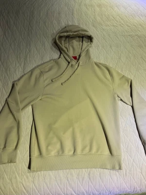 Beige hoodie från Hugo - Snygg beige hoodie från Hugo med diskret broderad logga på bröstet. Klassisk modell med huva och dragsnören samt ribbade muddar vid ärmar och nederkant. Perfekt för en avslappnad och stilren look. Kan passa M också.