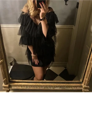 Svart volangklänning - Säljer en svart kortklänning med flera lager volanger och meshdetaljer upptill. Klänningen har offshoulder-design och är tillverkad i syntetmaterial. Finns ingen storlek i klänningen, men passar perfekt för mig som normalt har S(är 168) INTE MINA BILDER! Skriv för fler bilder😚