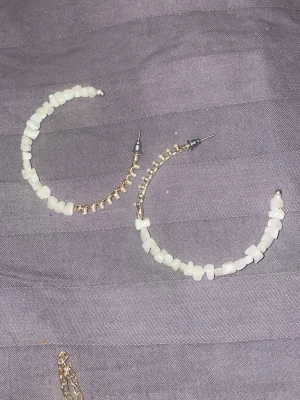 Guldiga hoops med vita pärlor - Säljer ett par stora hoops i guldmetall dekorerade med oregelbundna vita pärlor. Örhängena har en trendig och unik design som sticker ut. Perfekta för att ge din look lite extra edge.
