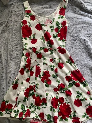 Vit klänning med röda rosor - Super söt vit röd blommig klänning, inte använt den på några år. Stl 32, vet inte vart den är ifrån så därav pris. ❤️
