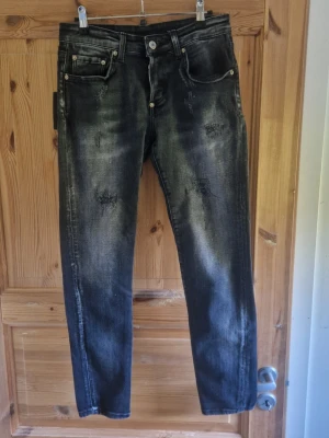 Svarta slitna jeans med tvättad look - Säljer ett par svarta jeans med tvättad och sliten look. Jeansen har raka ben, fem fickor och slitningar på flera ställen för en trendig vibe. Materialet är klassisk denim i bomull. Perfekta för dig som gillar en avslappnad och edgy stil.