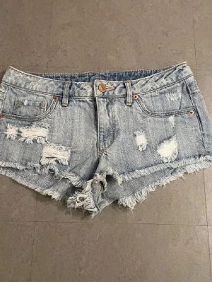 Ljusa jeansshorts med slitningar - Snygga ljusblå jeansshorts med råa kanter och slitna detaljer framtill. Klassisk femficksmodell med bälteshällor och knappstängning. Perfekta för varma dagar och en avslappnad stil.