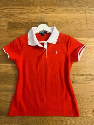 Röd polo t-shirt från Polo Ralph Lauren vintage - Snygg röd polo t-shirt från Polo Ralph Lauren med vit krage och korta ärmar. Ikonisk logga broderad på bröstet. Klassisk passform och tillverkad i mjuk bomull. Perfekt för dig som vill ha en stilren och sportig look.