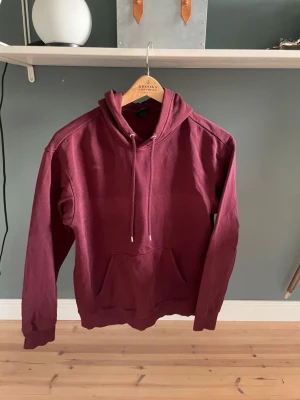 Vinröd hoodie från H&M Loose Fit - Snygg vinröd hoodie från H&M i loose fit-modell. Hoodien har huva med dragsko, känguruficka framtill och ribbade muddar vid ärmslut och nederkant. Tillverkad i mjukt bomullsmaterial som är skönt att bära. Perfekt för en avslappnad och trendig look.