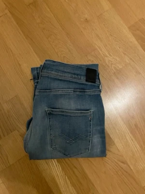 Blå slim fit jeans med bakfickor - Snygga blå slim fit jeans med klassiska bakfickor och diskreta slitningar. Jeansen har en enkel design med svarta patchdetaljer vid linningen och är tillverkade i stretchigt denim för en bekväm passform. Perfekta för en avslappnad och trendig look. Ny pris 1600kr W28/L32