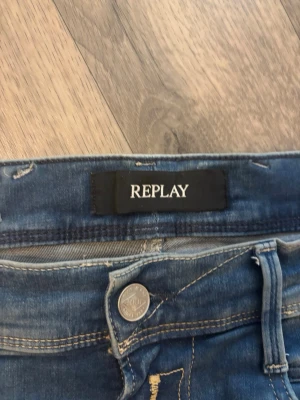Replay Anbass slim fit jeans blå - Säljer ett par Replay Anbass slim fit jeans i klassisk blå denim. Jeansen har snygga slitningar, fem fickor och silverfärgad knapp med Replay-logga. Materialet är mjuk och stretchig denim som sitter skönt och följer kroppen. Perfekta för en avslappnad och trendig look.