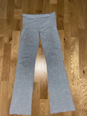 Gråa yoga pants - Säljer ett par grå leggings med bootcut-ben och låg midja. De är tillverkade i ett mjukt och stretchigt material som sitter skönt på kroppen. Perfekta för en avslappnad och trendig look. Liten fläck därbak som kanske går bort, men syns inte eftersom man viker ner