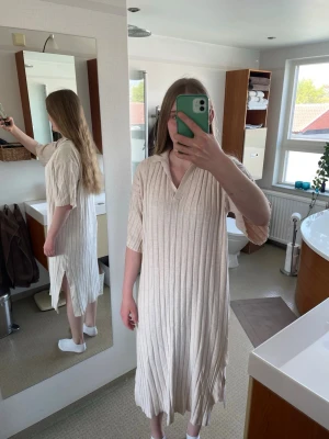 Stockholm LM - Snygg beige långklänning med ribbat mönster och slitsar på sidorna. Klänningen har v-ringning, krage och korta ärmar. Perfekt för en avslappnad och trendig look. Storlek S, men passar mer som en M