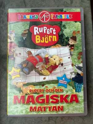Rupert Björk & den magiska mattan dvd - DVD-film med "Rupert Björn och Den Magiska Mattan". Innehåller 6 magiska äventyr. Speltid: 1 timme.  Finns på språk: Svenska, Norska, Finska   OBS!! skivorna är begagnade så det kan förekomma repor/hairlines på skivorna, men då jag kollar igenom alla filmer jag säljer garanterar jag att alla funkar felfritt om inget annat står! :)