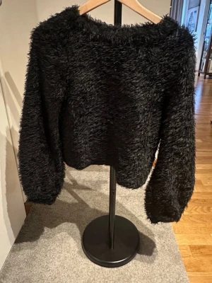 Svart lurvig stickad tröja XS Gina Tricot - Mysig svart stickad tröja från Gina Tricot i storlek XS. Tröjan har en fluffig och lurvig textur, rund halsringning och långa ärmar. Perfekt för att hålla sig varm och snygg under kyliga dagar.