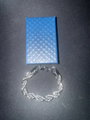 Silverplaterad cordell armband - Snyggt armband i silverfärg med tvinnad kedja och robusta lås. Kommer i en blå, quiltad ask. Perfekt accessoar för att lyfta din stil med en modern touch.