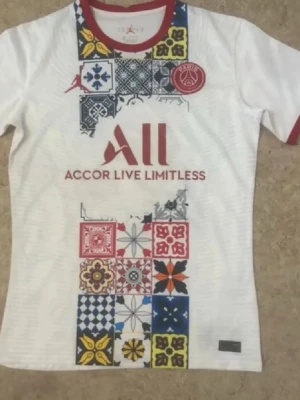 PSG x Jordan vit t-shirt med mönster - Snygg vit t-shirt från Jordan x PSG med färgglada grafiska mönster framtill och röd logga. Röd krage och ärmslut ger en sportig touch. Perfekt för dig som gillar fotboll och streetwear.