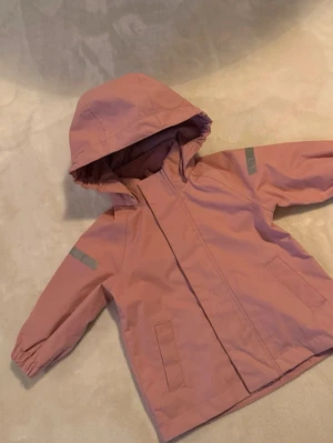 Rosa vindjacka med huva - Skaljacka från Lindex i storlek 74.  Den är för stor för min dotter än, endast använd två ggr så i nyskick🌸 Har inte tvättat den.   • Vattentätt material med minst 10 000 mm vattenpelare* Tejpade sömmar som gör plagget vattentätt Andningsförmåga på minst 5 000 g/m²/24h* Vindtätt material som stänger ut blåsten  Nypris 499:-
