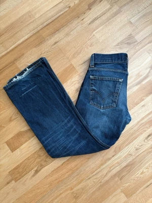 Mörkblå bootcut jeans från Levi's - Säljer ett par mörkblå bootcut jeans från Levi's med klassiska fem fickor och slitna detaljer vid bensluten.
