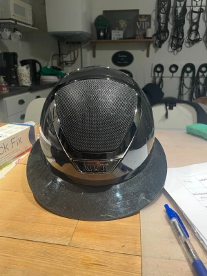 Svart ridhjälm från KASK - Snygg svart ridhjälm från KASK med ventilerande meshpanel framtill och blanka detaljer. Inköpt på Falsterbo 2024. Inte mycket använd. Originalkartong och hjälmväska följer med. Aldrig avramlad i.