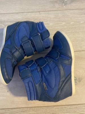 Blåa höga sneakers med kardborre - Snygga blå sneakers från Pax med högt skaft och tre kardborreband. Skorna har en kombination av textil och syntetläder, samt vit sula. Perfekta för dig som gillar sportig och modern stil.