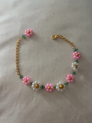 Blommigt pärlarmband med gulddetaljer - Ett armband med blommönster gjort av pärlor i rosa, vitt och grönt