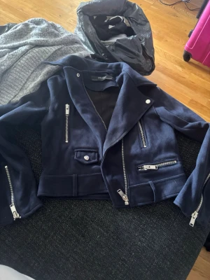 Mörkblå jacka från Zara Basic - Snygg mörkblå bikerjacka från Zara Basic med flera silvriga dragkedjor och detaljer. Jackan har bred krage, asymmetrisk dragkedja och är tillverkad i ett mjukt tyg som ger en cool look. Perfekt för dig som vill ha en stilren och trendig jacka.