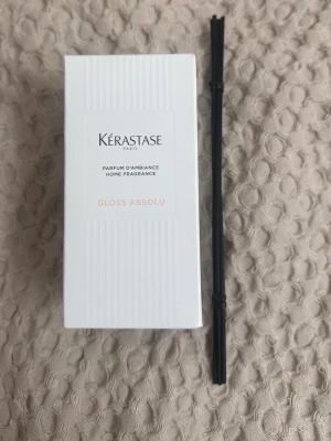 Kérastase Gloss Absolu doftspridare - Säljer en Kérastase Gloss Absolu doftspridare för hemmet. Setet innehåller en stilren glasflaska med räfflad yta och svarta doftpinnar. Förpackningen är vit med subtila detaljer och modern design. Perfekt för att ge rummet en fräsch och lyxig känsla.