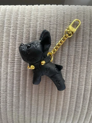  Vuitton hundnyckelring svart/guld - Säljer en svart hundformad nyckelring från Vuitton med guldfärgad kedja och detaljer. Nyckelringen har präglat LV-mönster och ett coolt nithalsband. Perfekt som accessoar till väskan eller nycklarna.