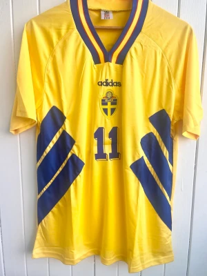 Tomas Brolin - Sverige - VM 1994 - Säljer en klassiska fotbollströja, Tomas Brolin svenska hemmamatchtröja från VM 1994 i USA. Tröjan är en reprint i nyskick.  Aldrig använd.  Storlek: Medium 