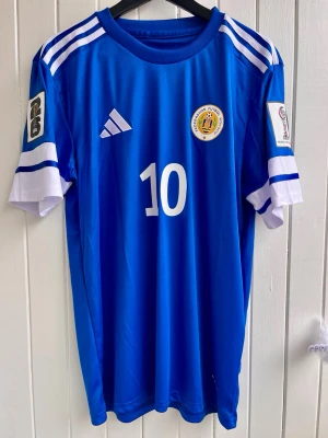 Bacuna - Curaçao - VM 2026 - Säljer en härlig fotbollströja inför stundande fotbolls-VM, nämligen Curaçaos matchtröja med lagkapten Bacuna på ryggen. Tröjan är en reprint i nyskick. VM 2026-patches. Large
