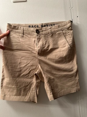 Beige shorts från Race Marine - Snygga beige shorts från Race Marine med klassisk passform. De har bälteshällor, knapp och dragkedja framtill samt fickor både fram och bak. Perfekta för varma dagar och enkla att matcha med olika outfits. Den är nästan oanvänd. 