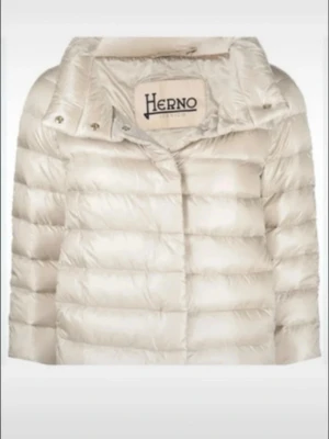Henro jacka ljusbeige  - Snygg ljusbeige dunjacka från Herno med bred krage och quiltad design. Jackan har en stilren look med diskreta knappar och är tillverkad i glansigt material som ger en exklusiv känsla. Perfekt för lager-på-lager-stil under kyliga dagar 💖