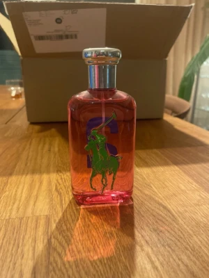 Ralph Lauren Big Pony 2 parfym - Cool parfym från Ralph Lauren Big Pony Collection, nummer 2. Flaskan är rosa med en stor blå tvåa på baksidan och grönt polospelmotiv på framsidan. Snygg metallkork och modern design – perfekt för dig som gillar färgstarka detaljer.