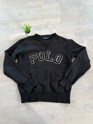 Svart sweatshirt från Polo Ralph Lauren - Svart sweatshirt med broderad POLO-text framtill. Klassisk rund halsringning och ribbade muddar vid ärmslut och nederkant. Perfekt för en avslappnad och stilren look.