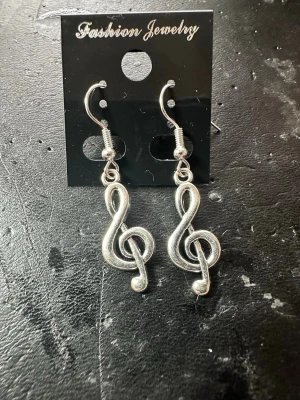 Silvriga örhängen med g-klav - Coola silvriga örhängen i form av g-klavar, perfekta för dig som älskar musik. Hängande modell med krok, tillverkade i metall. Snygg accessoar som sticker ut och passar till många olika stilar.
