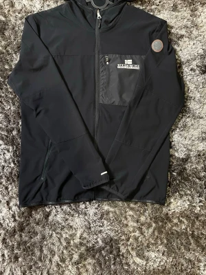 Napapijri jacka - Svart jacka från Napapijri. Aldrig använd, helt ny i perfekt skick. Inga märken eller skador. Skön och lätt jacka med huva och fickor. Passar bra till vardag och lättare kyligt väder. Mer bilder finns om det behövs. Kan gå ner i pris vid snabb affär