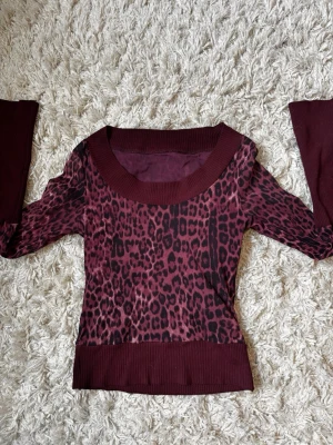 Vinröd leopardmönstrad tröja - Cool vinröd tröja med svart leopardmönster och bred ribbad mudd vid hals, ärmslut och nederkant. Tröjan har lång ärm och en figurnära passform, perfekt för dig som vill sticka ut lite extra.