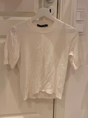 Vit kortärmad topp från 157 - En enkel och stilren vit topp från 157 med rund halsringning och korta ärmar. Toppen har en mjuk och lätt ribbad struktur som gör den bekväm att bära. Perfekt att matcha med jeans eller kjol för en clean look.