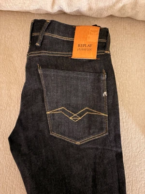 Replay Hyperflex mörkblå jeans - Säljer ett par mörkblå Replay Hyperflex jeans med snygga kontrastsömmar och unikt broderi på bakfickorna. Jeansen har klassisk femficksdesign och är tillverkade i stretchigt denim för extra komfort. Perfekta för dig som gillar stilrena och moderna jeans.