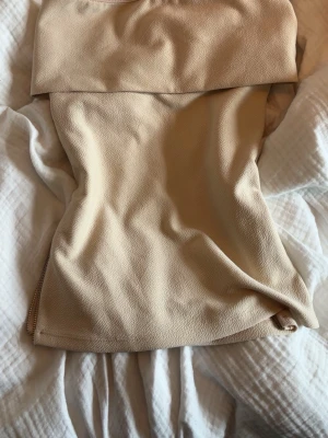 Beige axelbandslös topp från Zara - Snygg beige axelbandslös topp från Zara i en tight passform. Toppen har en bred kant upptill och är tillverkad i ett mjukt, lätt strukturerat material som känns lyxigt. Perfekt att styla med jeans eller kjol för en trendig look.