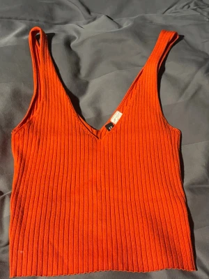 Ribbad orange linnetopp från H&M - Snygg ribbad orange linnetopp från H&M:s Divided-kollektion. Toppen har v-ringning och breda axelband, perfekt för varma dagar eller lager på lager. Enkel att styla med jeans eller kjol för en cool look. Linnet har en fläck som knappt syns.
