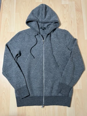 Kashmir hoodie med dragkedja  - Säljer nu denna snygga gråa kashmir hoodie från märket Theroy. Tröjan är i bra skick och har inga defekter.  När jag köpte den kosta den ca 2500 kr. Material: 91 % ull, 4 % kashmere och 5 nylon. Modellen på bilden är 183 och väger 67 kilo.  Skriv gärna om ni har någon fundering🙂