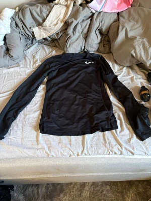 Svart långärmad träningströja Nike - Svart långärmad träningströja från Nike Pro med tight passform och diskret Nike-logga på bröstet. Tillverkad i ett stretchigt funktionsmaterial som andas, perfekt för intensiva träningspass eller löpning.