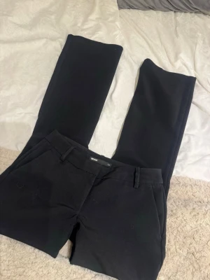 Svarta kostymbyxor från Bik Bok - Snygga svarta kostymbyxor från Bik Bok med raka ben och klassisk passform. Byxorna har hällor för skärp, sidofickor och stängs med dragkedja och knapp. Perfekta för en stilren look.