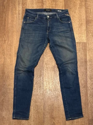 Mörkblå Slim Fit jeans från Replay (Katewin) 31/32 - Snygga blå skinny jeans från Replay med klassisk femficksmodell och läderpatch bak i midjan. Jeansen har diskreta slitningar och kontrastsömmar för en modern look. Materialet är mjukt och stretchigt för extra komfort. Storlek 31/32. Snabb Leverans!