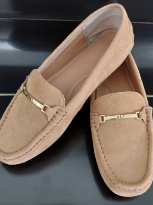 Beige mockaloafers från Ralph Lauren - Beige loafers i mocka från Ralph Lauren med guldfärgad metallbricka framtill där det står 'RLL'. Klassisk design med rundad tå och diskreta sömmar. Storlek 36 men smal i modellen. I nyskick.