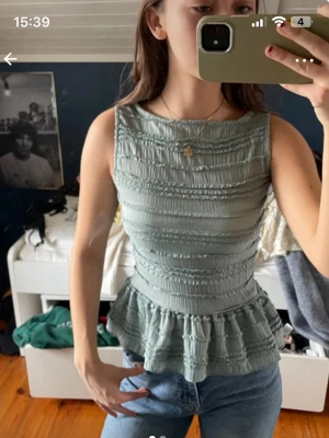 Grön ärmlös peplumtop - Säljer en ljusgrön ärmlös peplumtop med ribbad struktur och volang nedtill. Toppen har en tight passform och är perfekt att matcha med jeans. Materialet känns som bomull eller syntet.